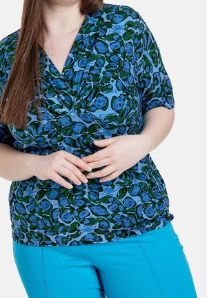 Blusa azul con patrones ovalados verdes, de manga corta y diseño de escote en V; combinada con pantalones azules. Textura de tela lisa.