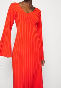 Robe rouge ajustée à manches longues avec un décolleté en V et une texture côtelée verticale, dotée de manches évasées et d'une finition en tissu lisse.