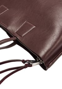 Bordowa skórzana torba o gładkiej fakturze, z zamkiem błyskawicznym i kontrastowymi zamszowymi paskami. Wyposażona w pasujące skórzane akcenty i dyskretne przeszycia.