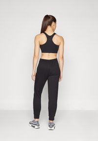 Black sports bra with racerback design, paired with loose black joggers and grey athletic shoes, showcasing a minimalist athletic look.