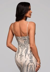 Robe de soirée perlée en ton nude avec des sequins argentés, silhouette ajustée, fines bretelles et détails de design floral délicat.