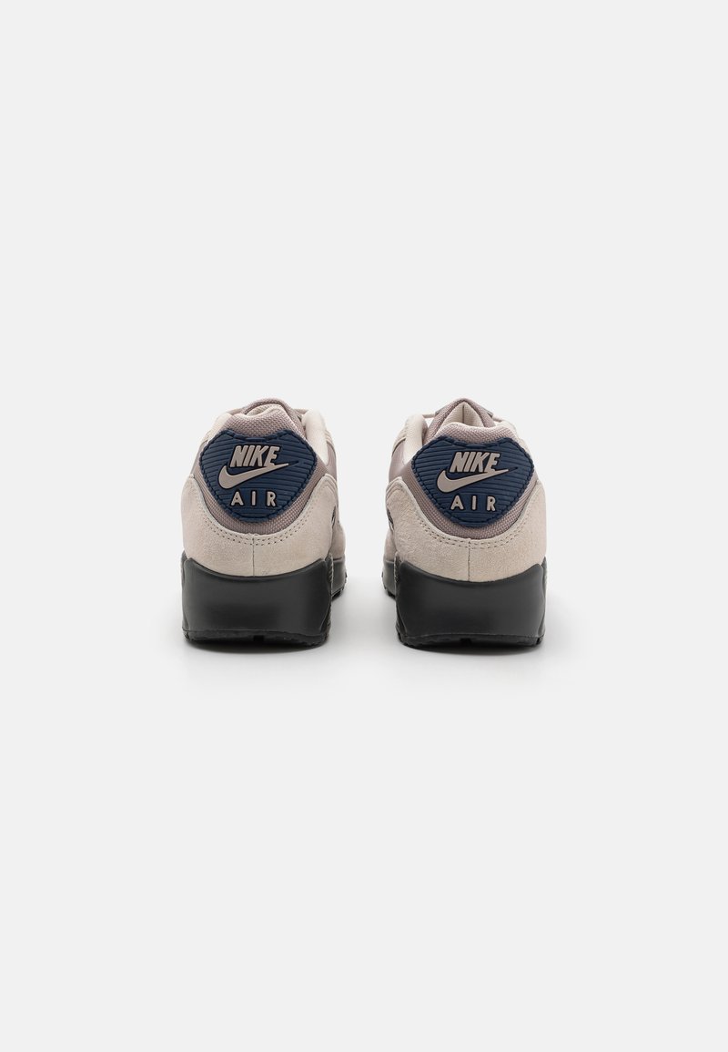 Nike Air Sneakers verfügen über ein beiges Wildleder-Obermaterial, eine marineblaue Fersenschlaufe mit Logo, eine schwarze Gummisohle und ein abgerundetes Zehendesign.