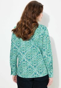 Blusa de flores verdes con estampado, de mangas largas, que presenta diseños intrincados en tonos de azul y un dobladillo recto.