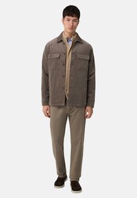 Brun manchesterjacka med fyra framfickor, bärs över en beige topp. Kombineras med ljusbruna byxor och mörkbruna slip-on skor.