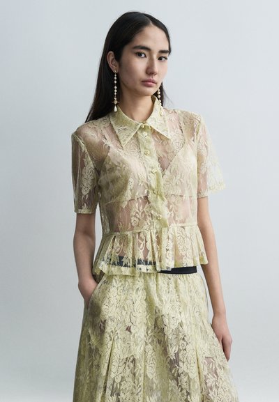 Haut en dentelle jaune clair, manches courtes, boutonné devant, design péplum. Présente des motifs floraux et une texture à couches, assorti à une jupe.