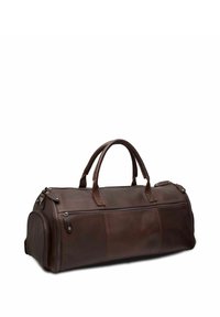 Bolsa de viaje de cuero marrón con forma redondeada, dobles asas y dos cremalleras. Presenta detalles de costura y un bolsillo frontal con cremallera.
