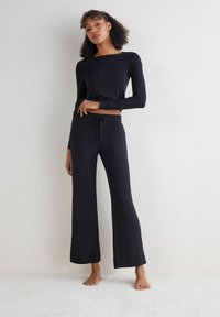 Top negro de manga larga combinado con pantalones amplios a juego. Ambas prendas presentan una textura suave y una cintura elástica con cordón.