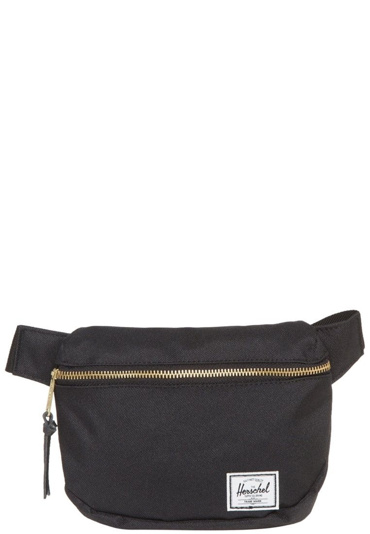 Musta kangaskotelo kultaisella vetoketjulla, etutaskulla ja valkoisella logotarralla. Muodoltaan suorakulmainen ja varustettu säädettävällä hihnalla.