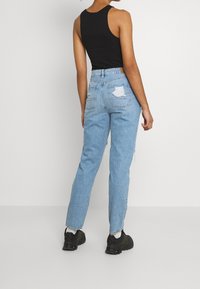 Jean déchiré bleu clair avec une coupe décontractée, doté de deux poches arrière et d'une taille moyenne. Porté avec un haut noir sans manches et des baskets noires.