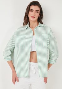 Green and white striped button-up shirt with two chest pockets, roll-up sleeves, and a relaxed fit, made of lightweight fabric.