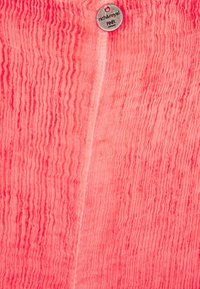 Tessuto rosa con texture caratterizzato da linee ondulate verticali, con un piccolo tag di metallo attaccato, etichettato "rich&royal PHA."