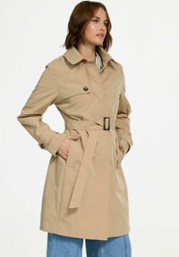 Beige trenchcoat met een ceintuur in de taille, twee voorke pockets en een kraag. Heeft knoopaccenten en een slank, op maat gemaakt ontwerp.