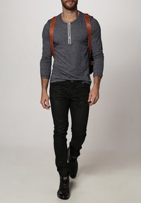 Tumma harmaan pitkähihaisen paidan nappikiinnityksellä, yhdistettynä mustiin farkkuihin ja mustiin saappaisiin. Ruskeat nahkaremmikäsis vyöhykkeellä viimeistelevät asun.