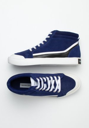 Een paar marineblauwe suède hoge sneakers met witte veters, witte rubberen zolen en zwarte strepen aan de zijkanten.