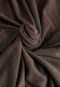 Tissu en tricot marron enroulé en spirale, mettant en valeur une texture douce et un tissage lisse et uniforme avec de légères lignes diagonales.