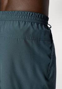 Bañadores de hombre en un tono verde azulado oscuro con cinturilla elástica, cordón y una textura suave. Cuenta con un bolsillo lateral y detalles de costura limpia.