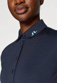 Polo de cor navy com colar estruturado, apresenta um logótipo bordado em azul claro, quatro botões e um tecido suave e texturizado.