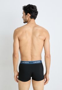 Boxers en coton noirs avec une ceinture de marque bleue, offrant une coupe ajustée et une texture lisse, portés par un mannequin masculin vu de dos.