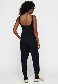 Top de tirantes negro acanalado con espalda baja, combinado con pantalones negros sueltos con corte tapered, que presentan puños elásticos y bolsillos laterales.