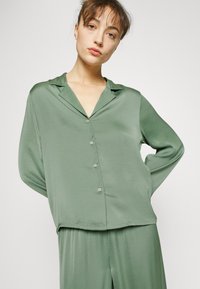 Grön satinbutton-up blus med krage, långa ärmar och avslappnad passform. Har små knappar och en slät, glansig yta.