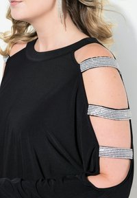 Schwarzes Oberteil mit Kalt-Schulter-Design, verziert mit silbernen Strassakzenten an den Schultern. Glattes Material, lockere Passform, lange Ärmel.