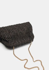 Sort clutch-tasken med perlebesat tekstur og bølget mønster, med en guldkæde som rem. Blødt stof med en samlet finish. Kompakt design.