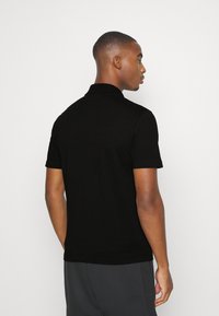 Černé polo tričko s límcem, krátkými rukávy a hladkým povrchem, s čistým, minimalistickým designem bez viditelných log nebo ozdob.