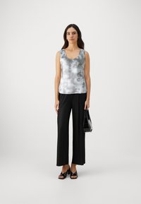 Satin, ärmelloses Top in Grau mit einem Batikmuster; kombiniert mit schwarzen, plissierten, weiten Hosen und schwarzen, hochhackigen Sandalen.