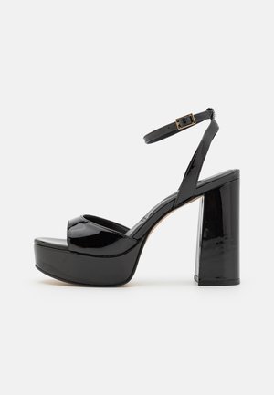 Black patent leather platform sandals with an ankle strap, featuring a chunky high heel and peep-toe design. Smooth texture and glossy finish.