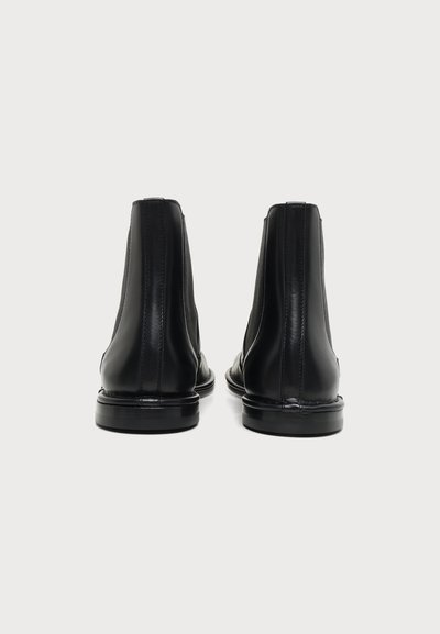 Paire de bottines en cuir noir vues de dos sur un fond clair uni.