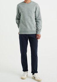 Ljusgrön sweatshirt med blommönster, rundad hals, ribbat manschett och nederkant, parat med mörkblå byxor och off-white sneakers.