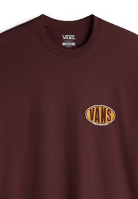 Burgundské bavlněné tričko s kulatým oranžovým a černým logem "VANS" na přední straně; zahrnuje kulatý výstřih a volný střih.