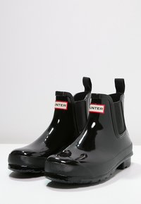 Czarne gumowe buty Chelsea z elastycznymi panelami po bokach i teksturowaną podeszwą, oznaczone czerwono-białą metką na cholewce.