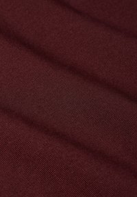 Bordeaux stof met een gladde textuur, met subtiele rek en fijne breiweef, toont een lichte rimpeling door het vouwen.