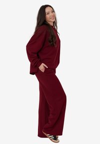 Burgundowa bluza o luźnym kroju i szerokie spodnie, wykonane z miękkiego materiału, w połączeniu z sandałami w czarno-białe paski.