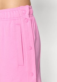 Detailný záber na osobu, ktorá má na sebe ružové tepláky s elastickým pásom, bočnou vreckom a cvokmi pozdĺž vonkajšieho švu.