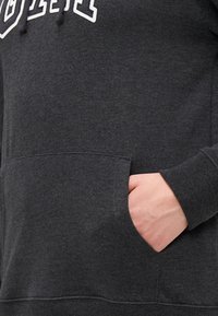 Tumši pelēks hoody ar kenguru kabatu, ribotām piedurknēm un auklu kapuci. Audums izskatās mīksts ar smalku tekstūru.