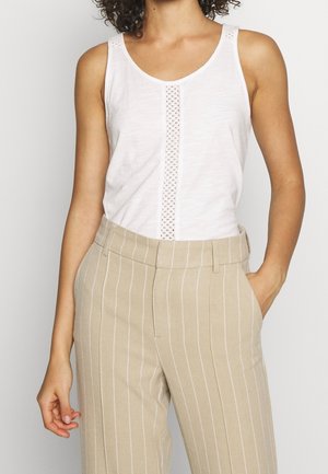 Débardeur blanc avec un panneau avant texturé, associé à un pantalon beige à rayures avec une coupe ajustée et des poches latérales.