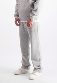 Grijze sweatpants met een ontspannen pasvorm, voorzien van een geborduurd logo op de linker bovenbeen, en gecombineerd met witte sportschoenen.