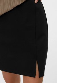 Falda negra ajustada con una pequeña abertura lateral, combinada con un top beige de canalé, que muestra parte de la cintura y el muslo superior.