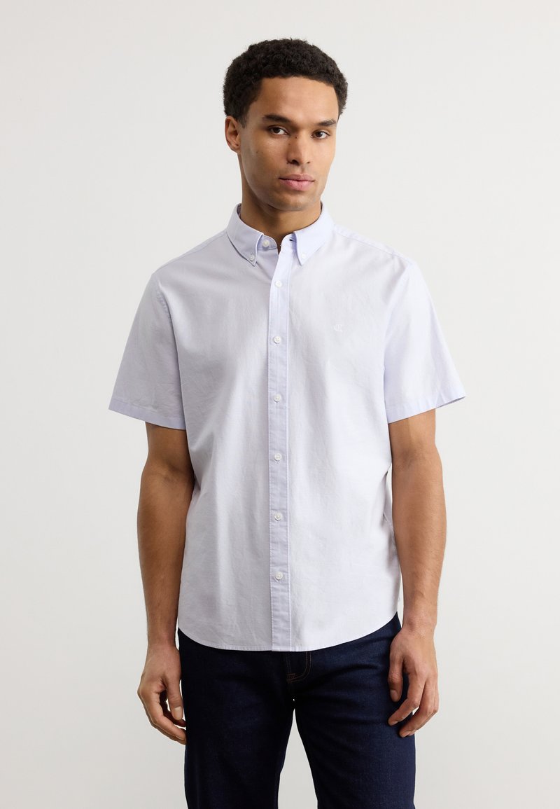 Ανοιχτό μπλε πουκάμισο με κοντά μανίκια και κουμπιά, κατασκευασμένο από βαμβάκι, με γιακά, διακριτικό λογότυπο στο στήθος και ίσια γραμμή κάτω.