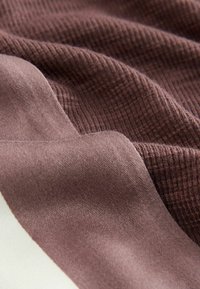 Měkká látka v hluboké mauve barvě, se hladkými a texturovanými sekcemi, vytvářející vrstvený vzhled s jemnými záhyby.