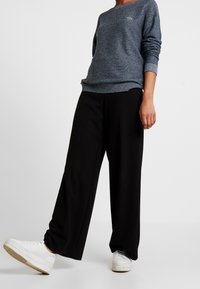 Sweat-shirt gris en tricot à manches longues et col rond, associé à un pantalon large noir et des baskets blanches.