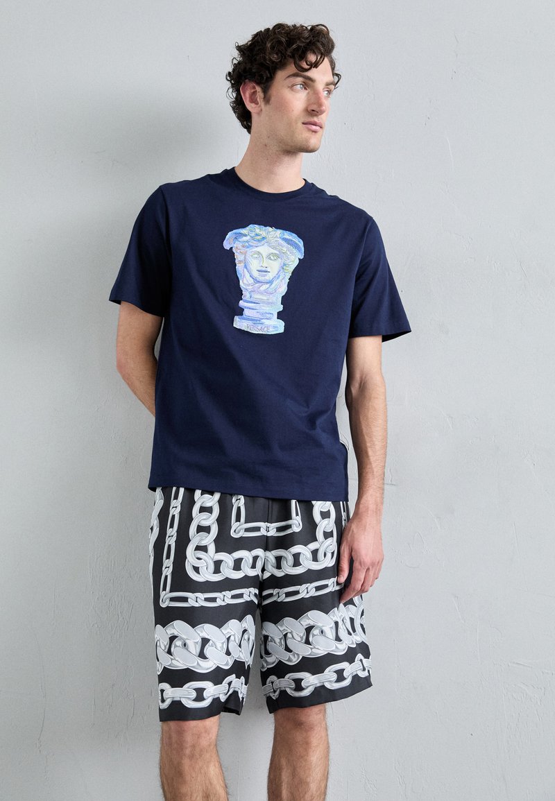 T-shirt en coton bleu marine avec un graphique coloré sur le buste. Associé à un short noir présentant un motif de chaînes blanches.