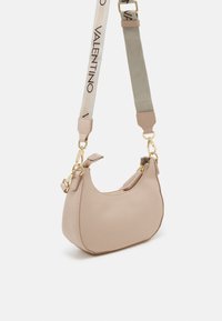 Bolsa de ombro de couro bege com um formato curvo, acessórios em dourado e uma alça destacável com um tecido estampado. Fecho de zíper em cima.