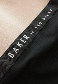Tessuto nero e beige con cuciture visibili. Presenta un'etichetta nera prominente con la scritta "BAKER by TED BAKER" in carattere sans-serif bianco.