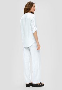 Chemise en lin légère, de couleur bleue claire, à manches longues et à ourlet arrondi, associée à un pantalon large bleu clair et à des sandales à plateforme noires.