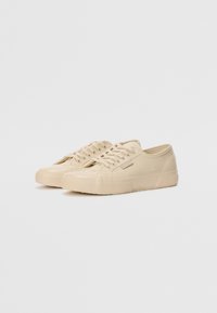 Beige gummisko med en glat tekstur, rund tå, snørebånd foran og en tekstureret sål for greb. Minimalistisk design med sideakcenter.