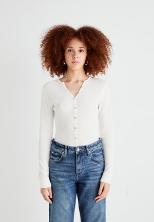 Langermet ribbestrikket cardigan i krem med gullknapp-lukking, kombinert med høy midje blå denim jeans.