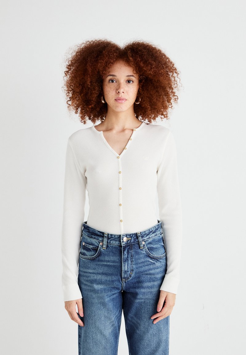 Langermet ribbestrikket cardigan i krem med gullknapp-lukking, kombinert med høy midje blå denim jeans.